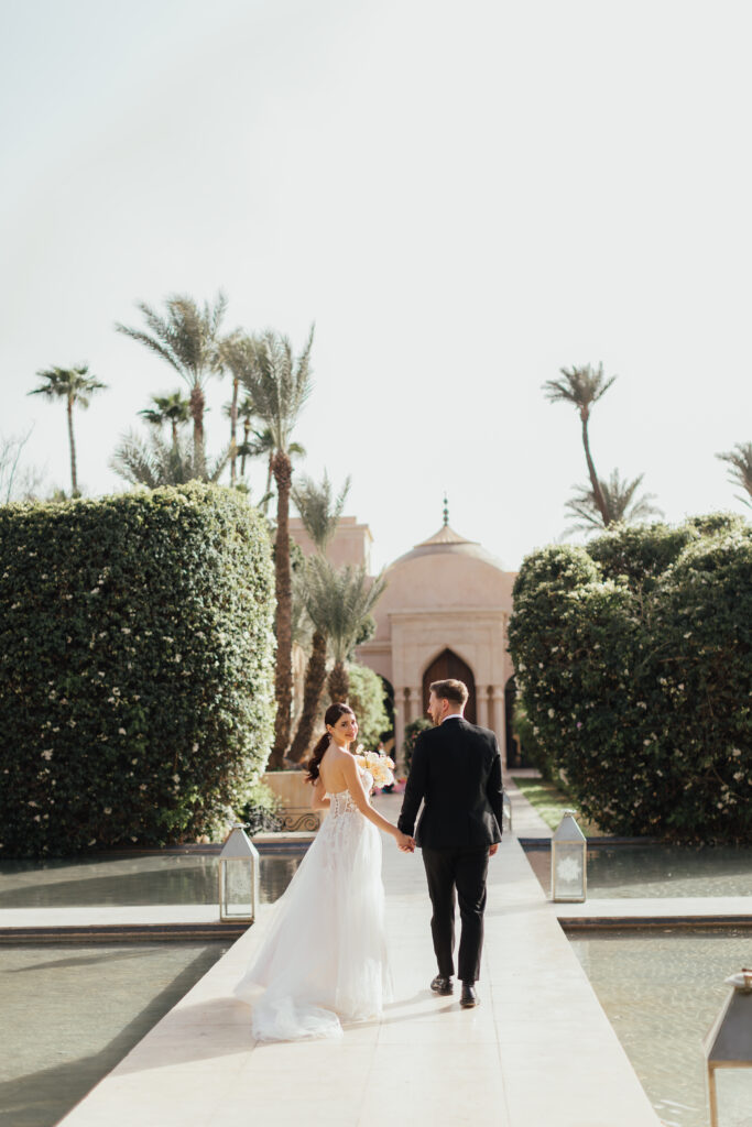 Couple walking hand in hand at their Marrakesh destination wedding with palm trees