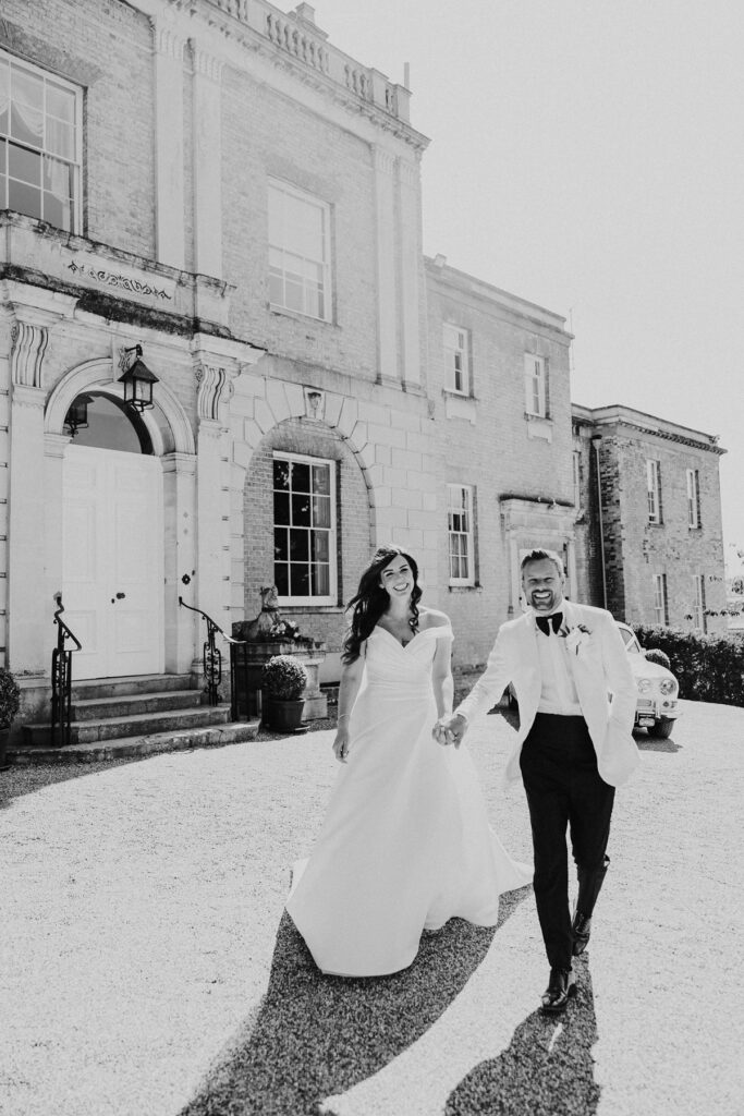 Essex Wedding Photographer capturing bride and groom laughing and walking hand in hand outdoors